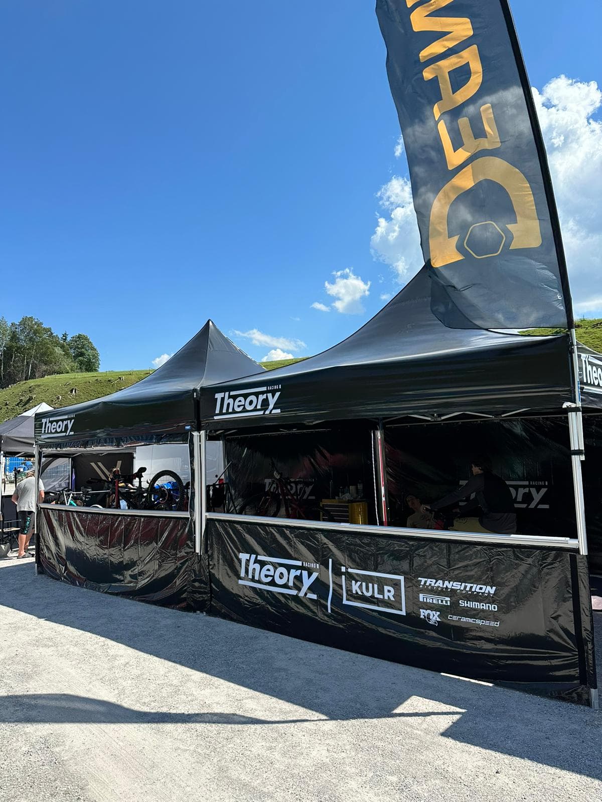 Black branded pop-up tents at an outdoor motorsport event with sponsor signage and mountain backdrop
